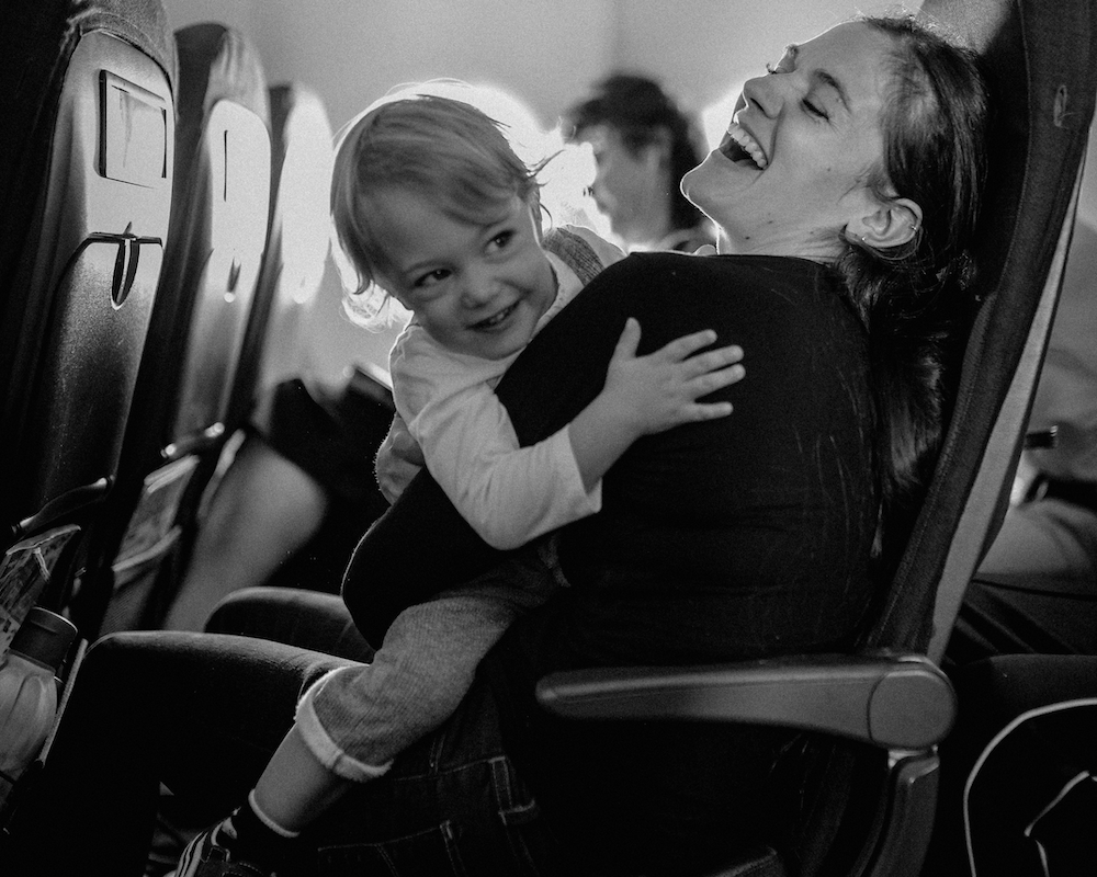 a mother holds a child on her lap in a plane; they're both laughing