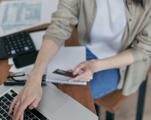 close-up of a woman holding a credit card and typing on a laptop while sitting at a desk with many documents