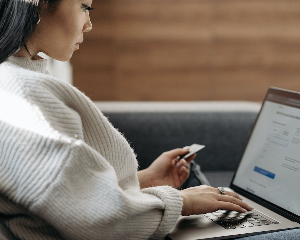 a woman holds a credit card while typing on a laptop