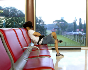 a passenger rests with a hat over his face while waiting in an airport