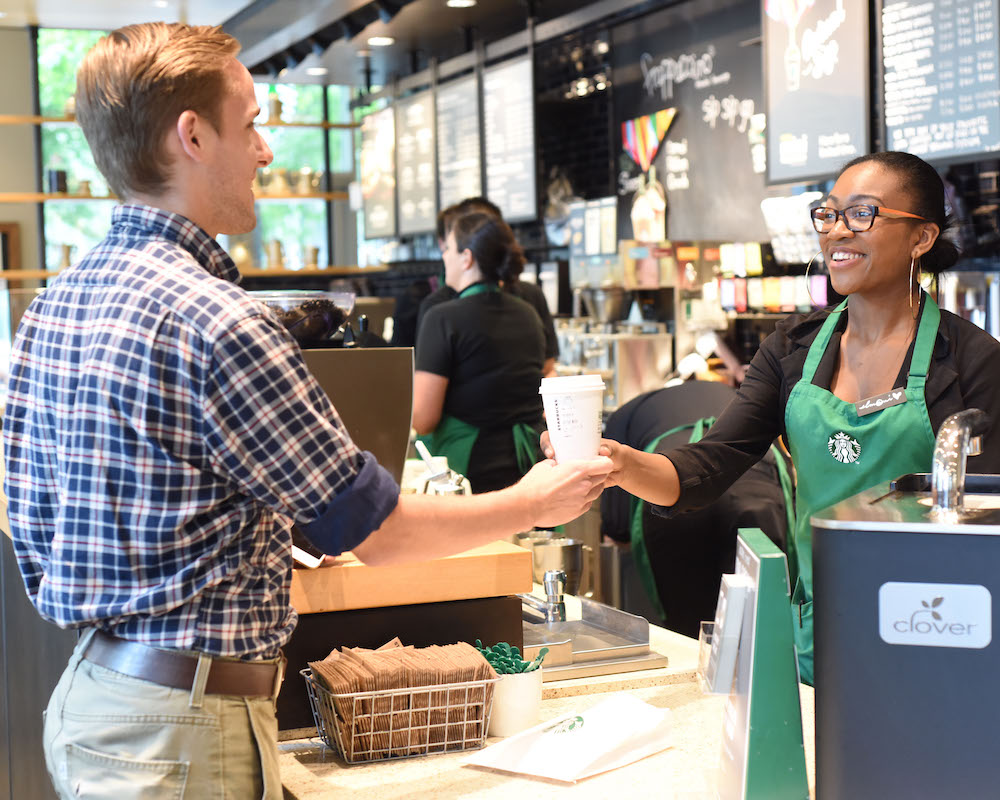 a Starbucks employee hands a drink to a customer inside a store