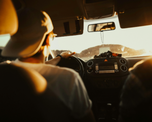 a guy with a backwards hat drives a car at sunset