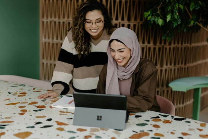 Two women look at a tablet screen with smiles on their faces.