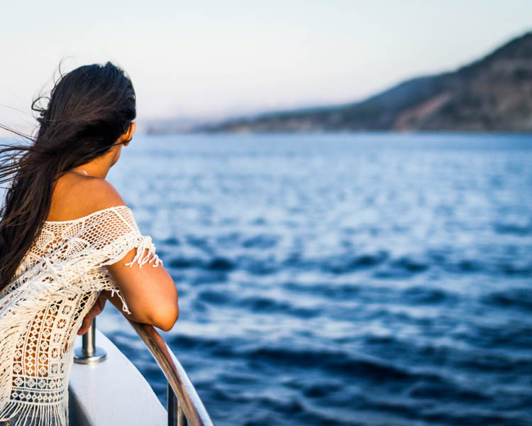 woman leaning on the railing of a cruise ship looking at the water