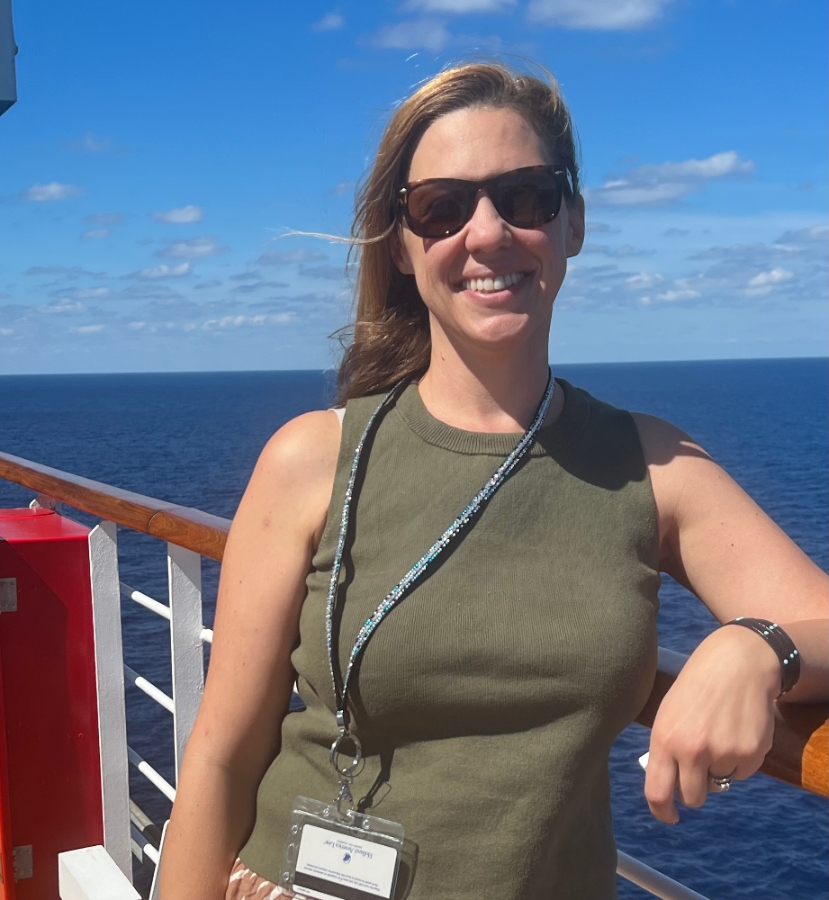 a smiling woman leans on the railing at the side of a cruise ship