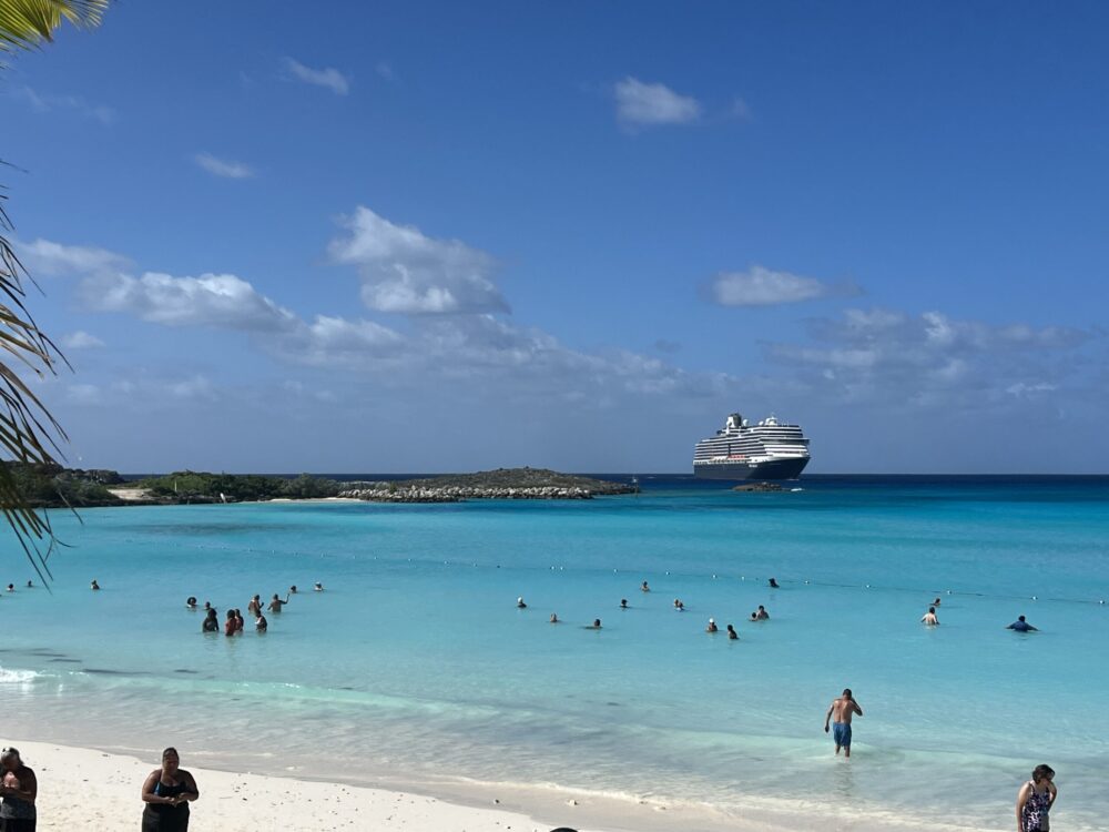 people swimming in the sea near a beach with a cruise ship in the background