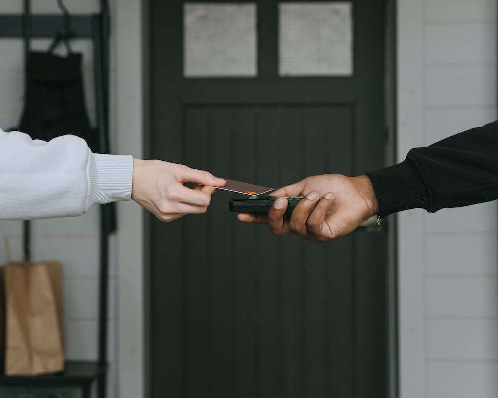 a close-up of a hand tap a credit card to a card reader held by a hand from a different person