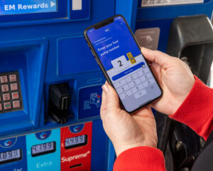 close-up of hands holding a smart phone showing the Walmart Plus app and entering a pump number for the gas discount