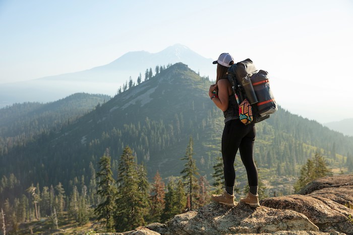 A woman with a hiking backpack looks out over a mountain.