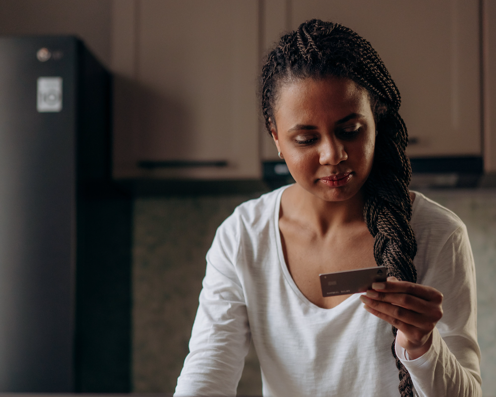 a woman stands in a kitchen looking at a credit card