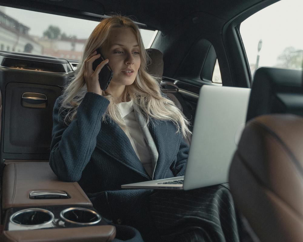 woman talking on phone in back seat of car while holding a laptop