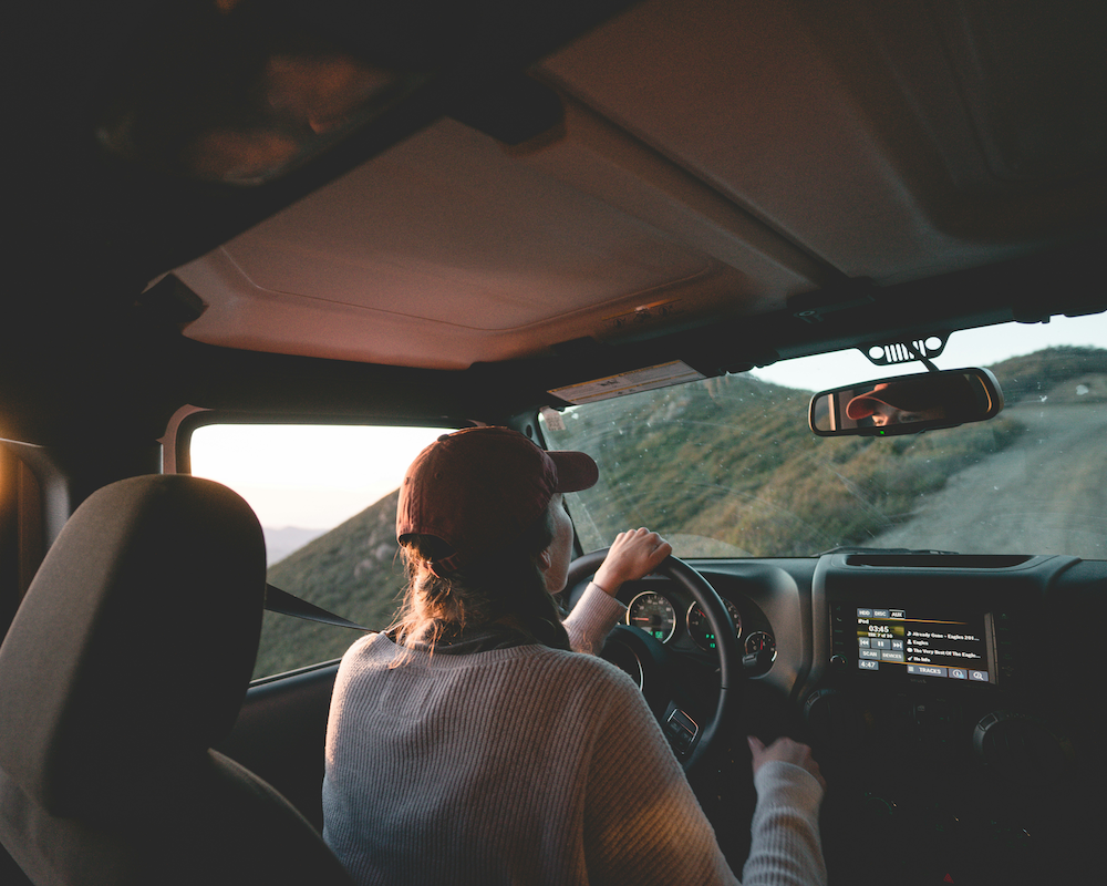 a young woman driving a car uphill on a dirt road