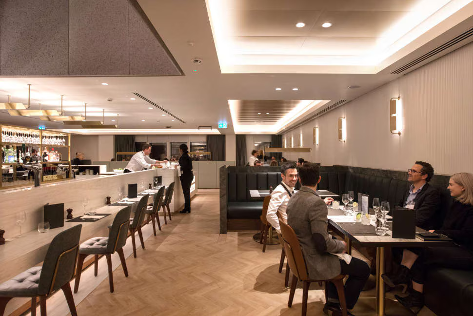 A restaurant style setup at the Qantas Lounge at London Heathrow. Passengers are seen at a table enjoying their visit.