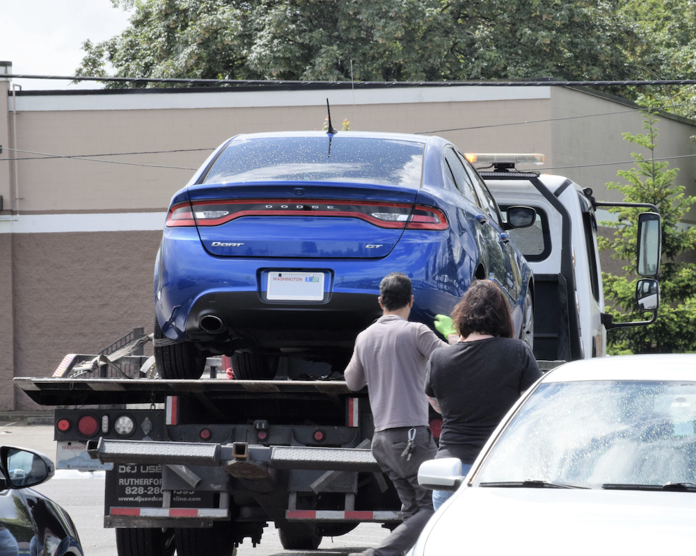 Blue car on the bed of a tow truck.
