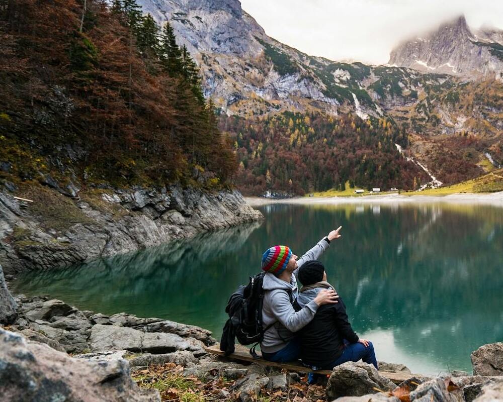 Couple sitting next to a lake with mountains in the background.