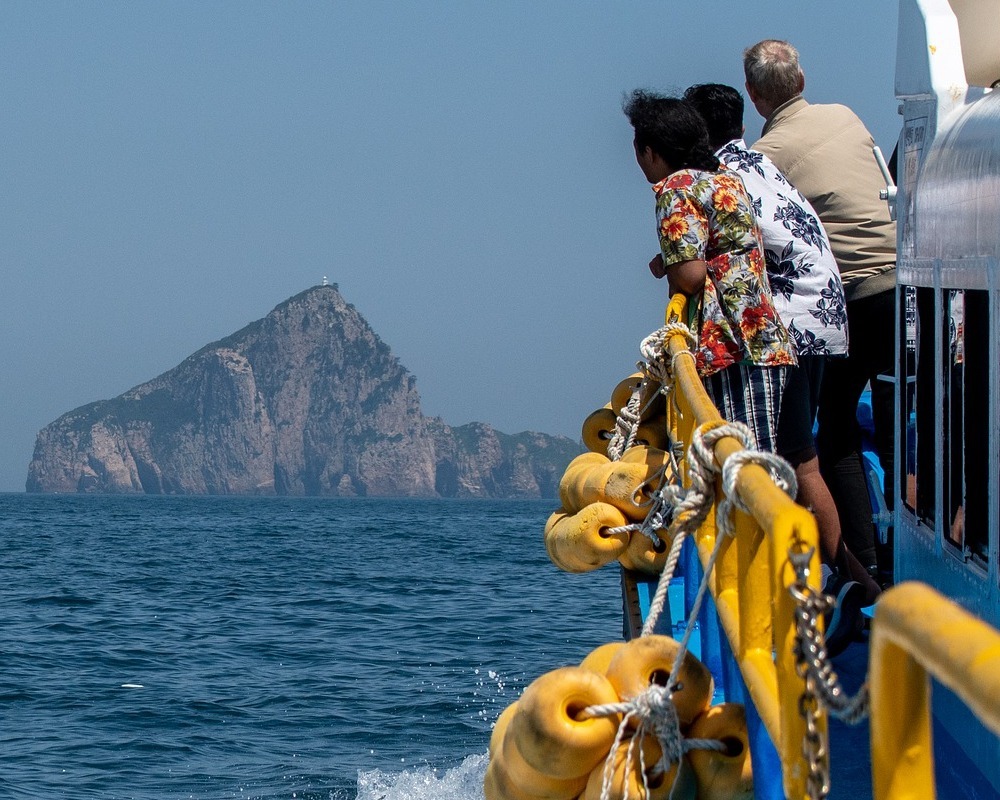 People leaning over the side of a boat to view the ocean and landmarks.