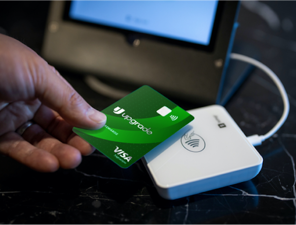 A hand holding an Upgrade Cash Rewards Visa card swipes at checkout.