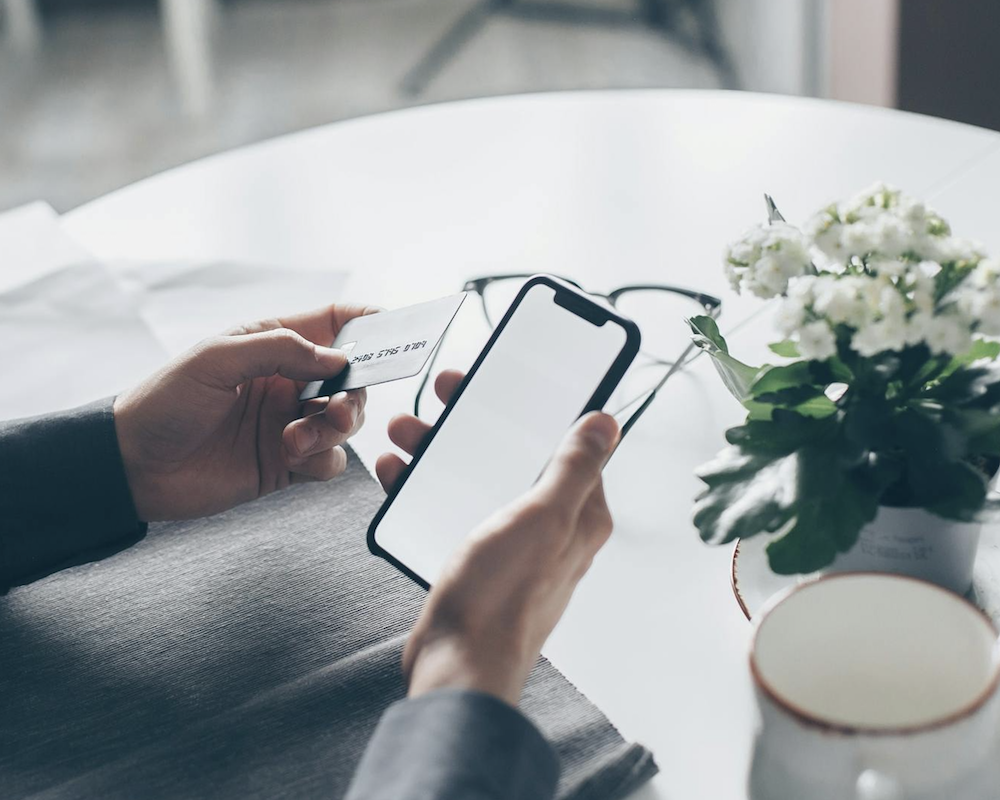 Man holding a credit card and looking at his cell phone.