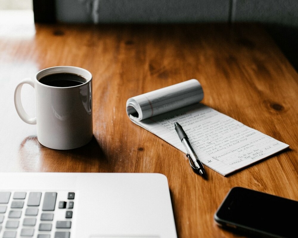 Notepad on a desk next to a cup of coffee.