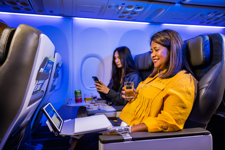 A woman sits in premium class on an Alaska Airlines plane with a glass of champagne in her hand and a laptop on her tray.