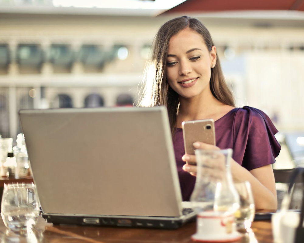 Woman holding a phone and looking at her laptop.