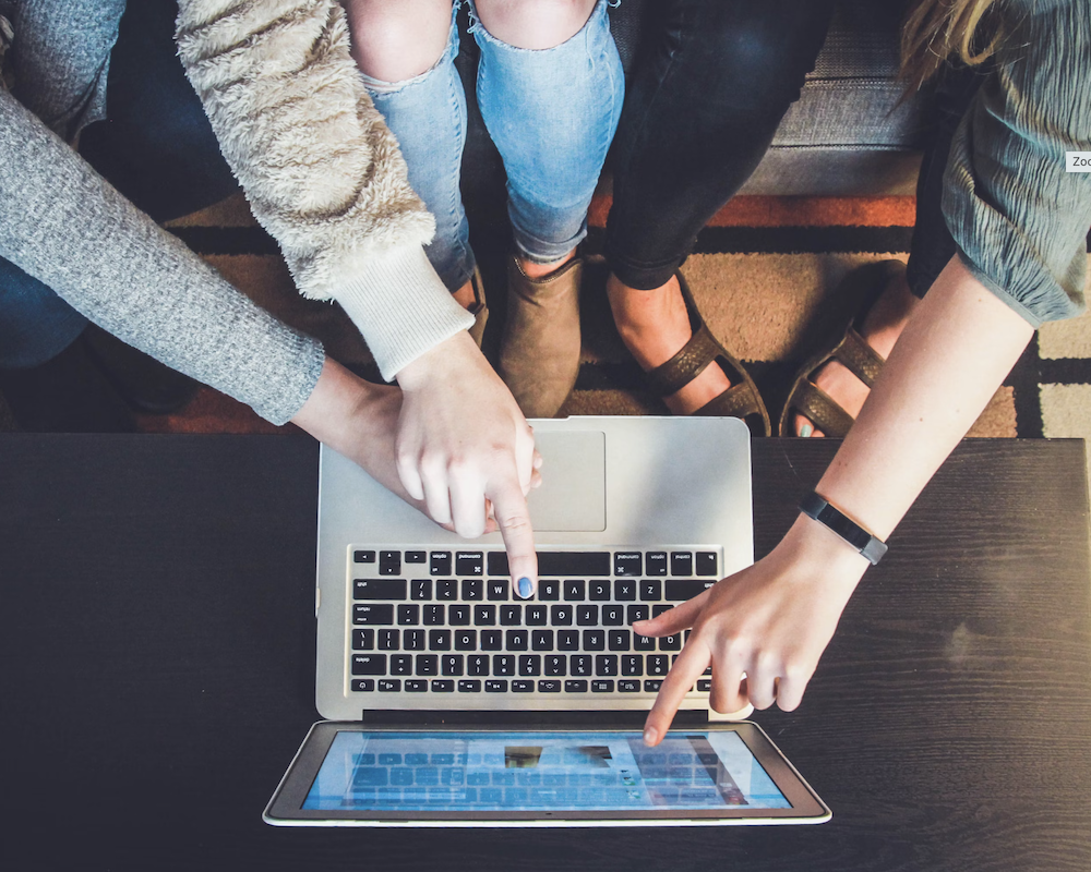 Overhead shot of three people pointing at a laptop screen.