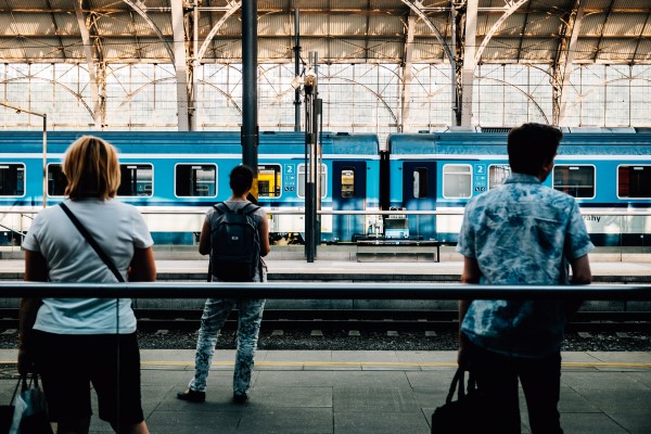 A photo of 3 people waiting on a train platform