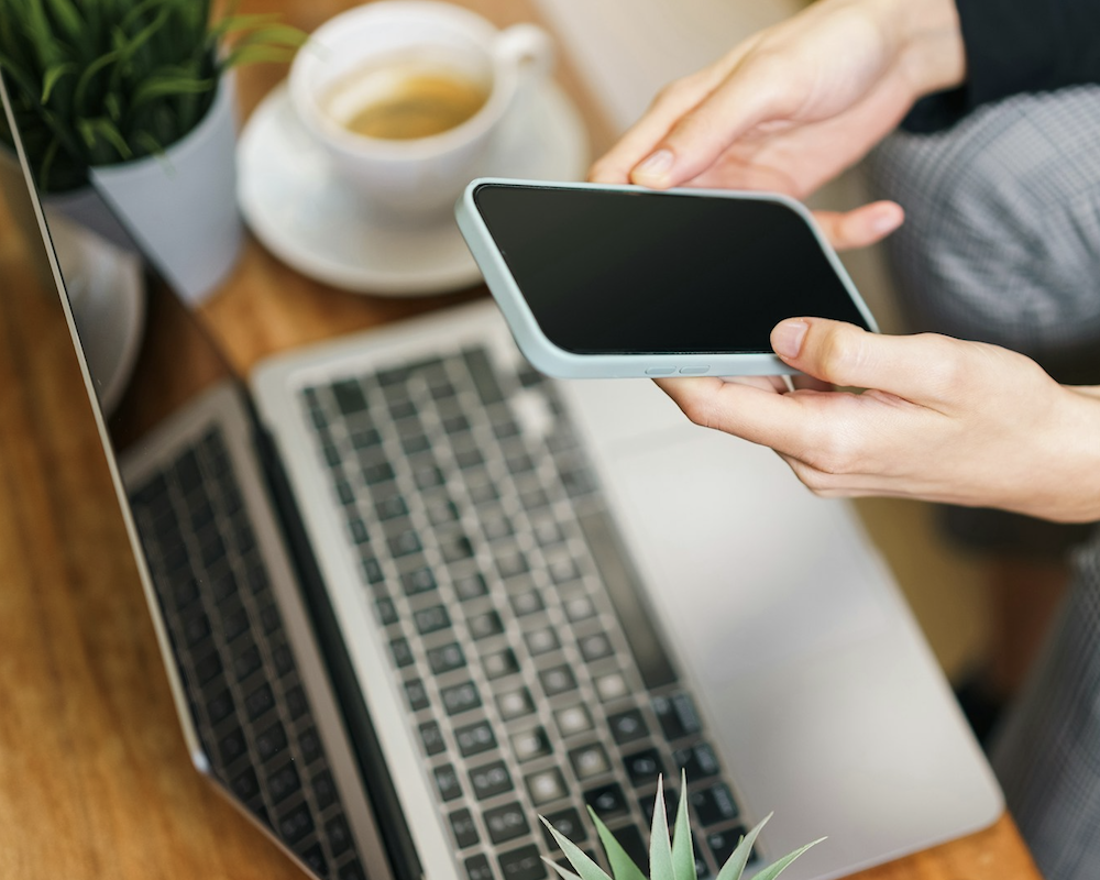 Woman holding an iPhone near a laptop.