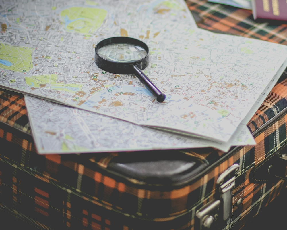 Map and a magnifying glass sitting atop a suitcase.