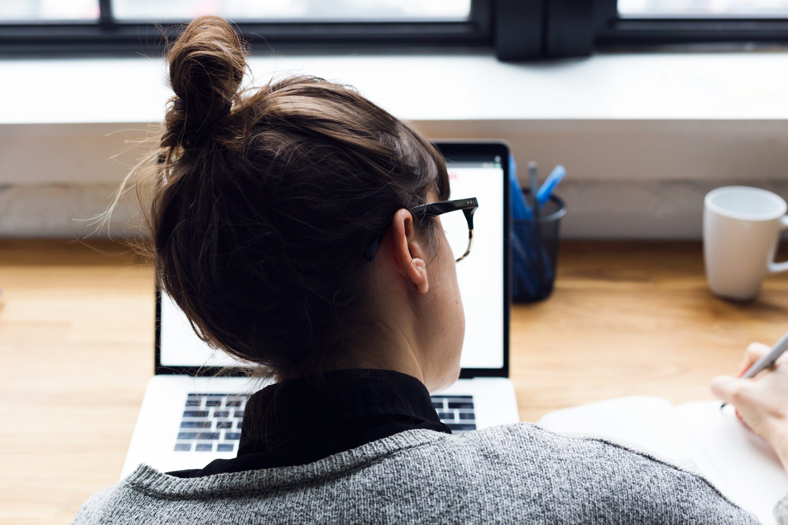 A photo shows a woman is taking notes and using a laptop