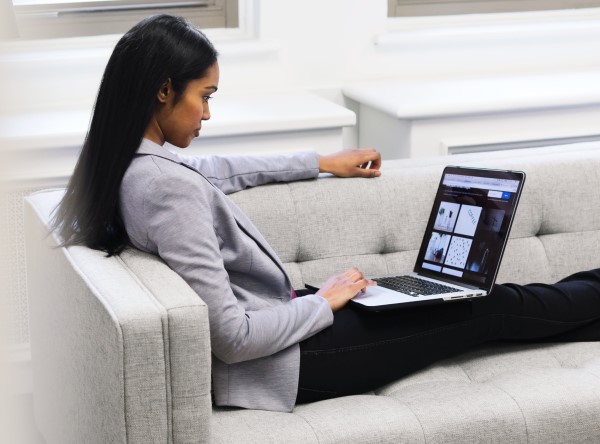 A photo of a woman sitting on a couch while scrolling on a laptop
