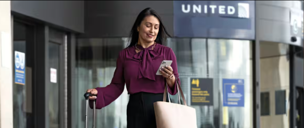 A photo of a woman on her phone outside of a United sign at an airport