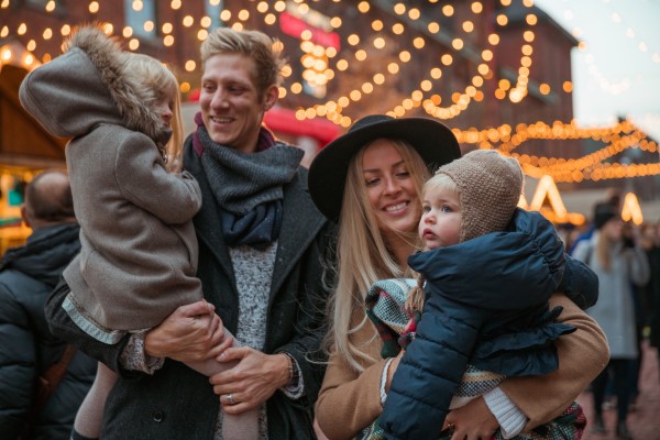 A family of 4 stands in front of a carousel at a Christmas Market.