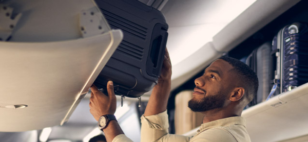 A photo shows a man putting a suitcase into the overhead compartments on a plane.