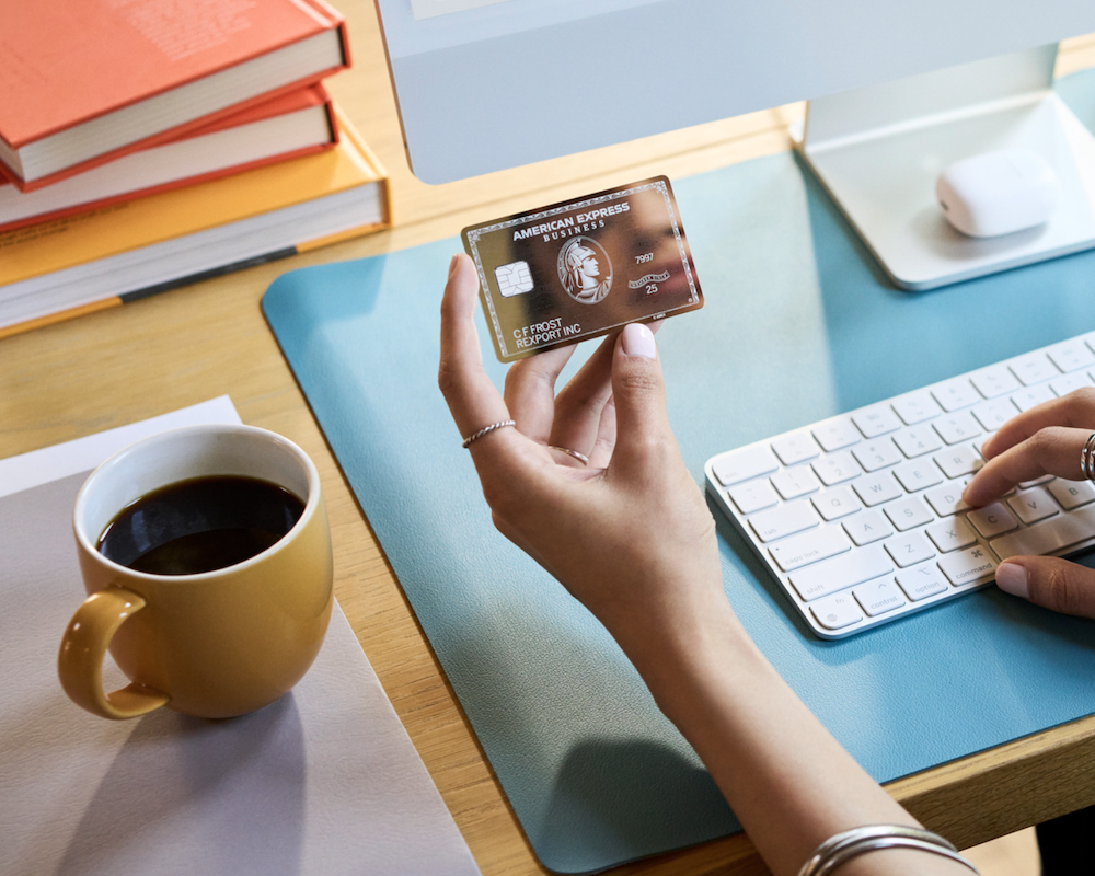 Woman holding the American Express Platinum Card while sitting at a desk.