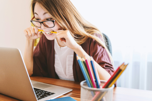 A woman is looking at her computer and biting a pencil.