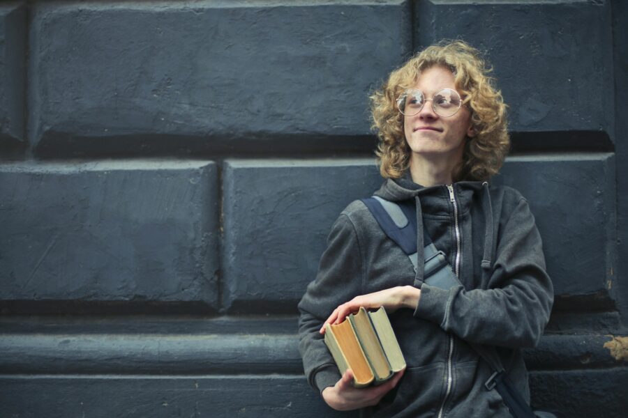 A college student standing in front of a wall holding books