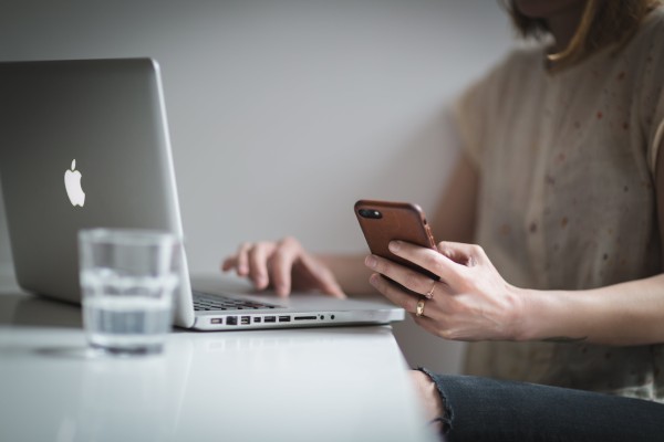 A photo of a woman checking her phone with a lap top open