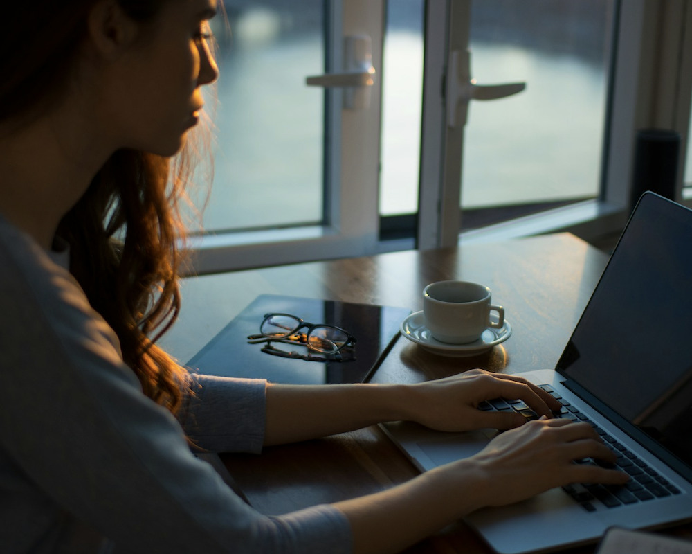 Woman working on a laptop in a dimly-lit office.