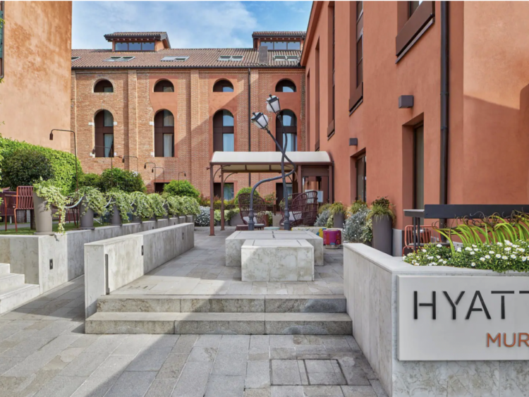 Concrete sidewalk with twisted lamps, terra cotta colored building, and part of the Hyatt Centric Murano sign