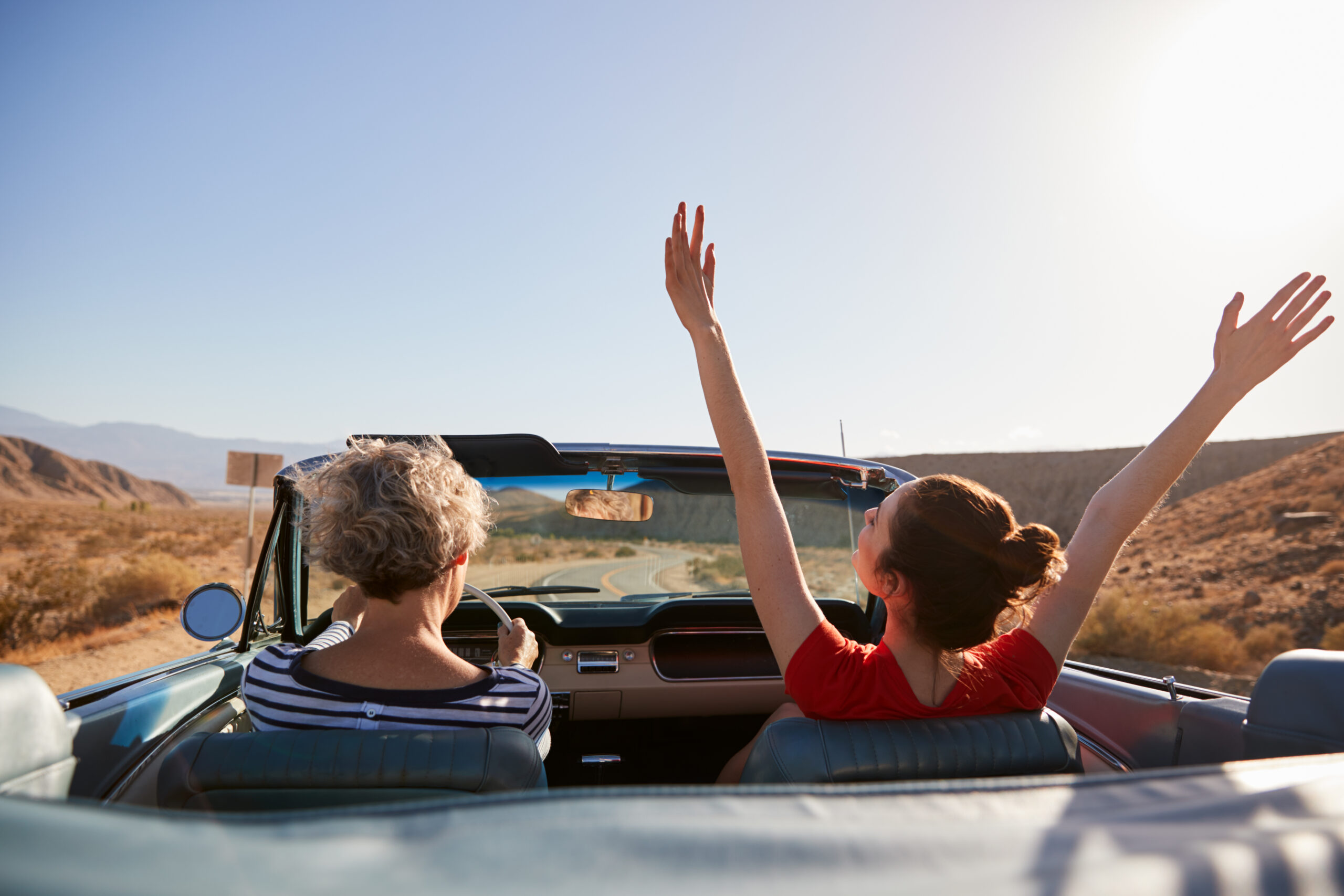 Grandmother driving car, daughter with hands in the air, back view