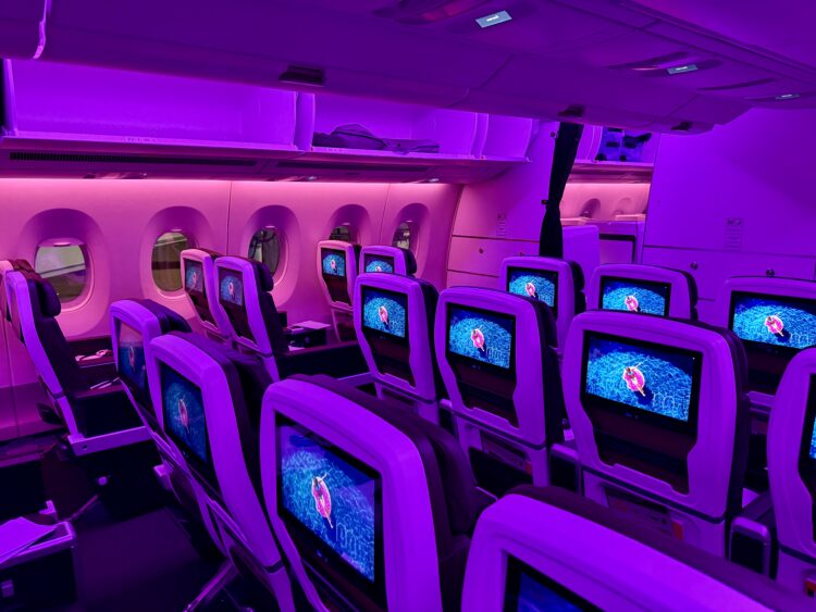 Airplane economy-class cabin with soft purple and fuschia lighting