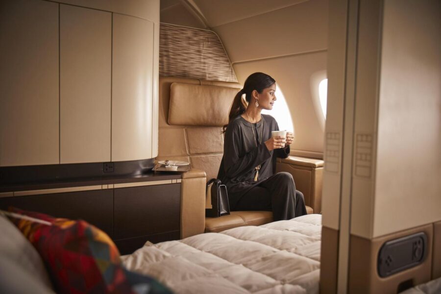 A woman seated in an Etihad Apartment first class suite holding drinking a beverage