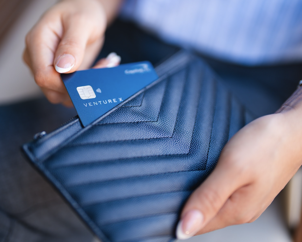 A hand pulling a Capital One Venture X out of a wallet.