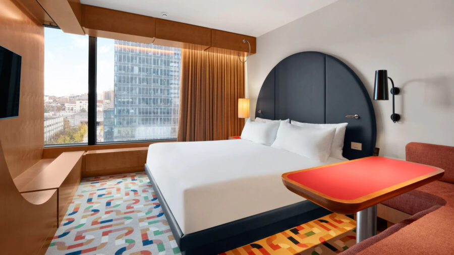 Room at The Standard Brussels with large bed in the middle surrounded by a colorful rug and large open window