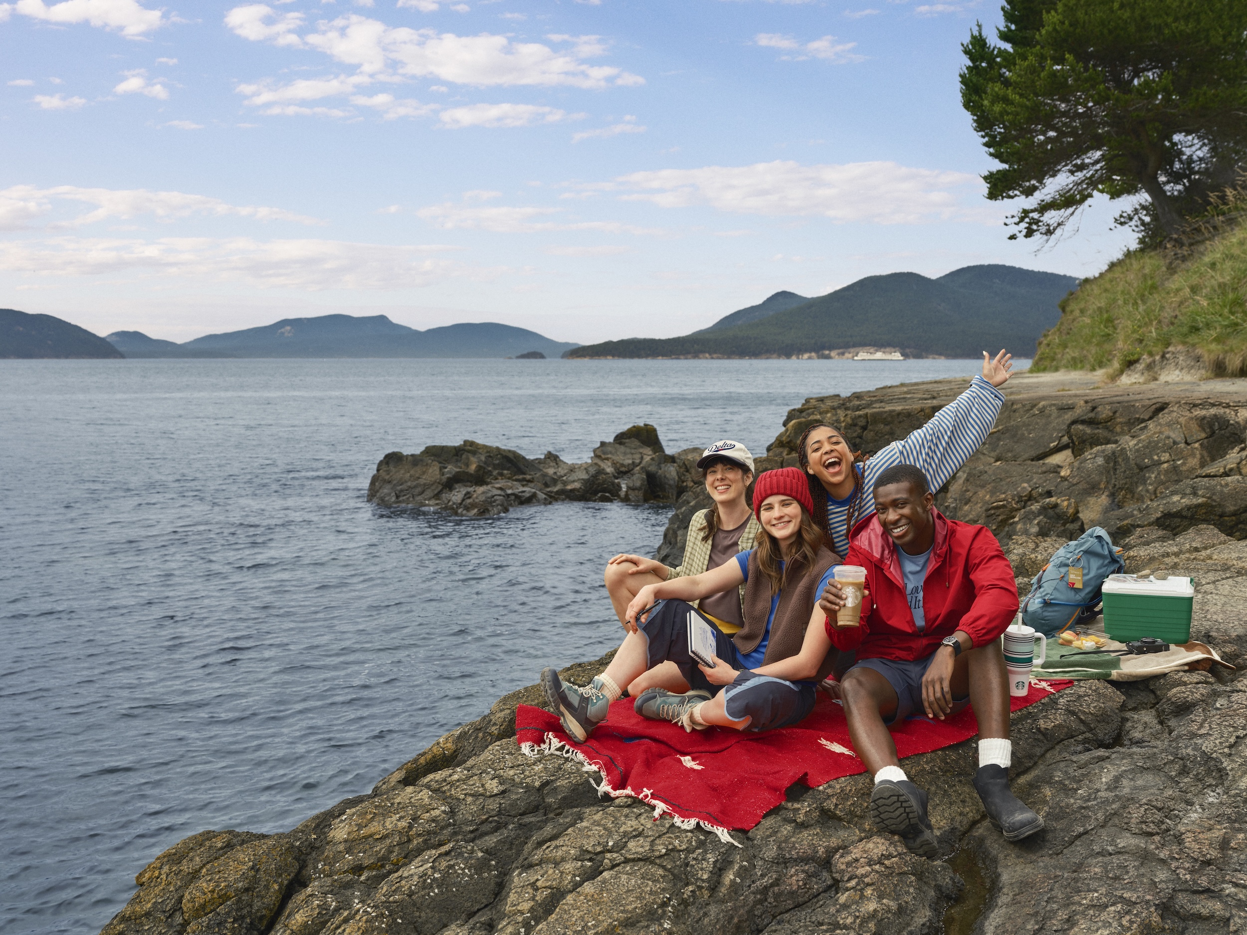 Four people on a rock by a lake holding Starbucks