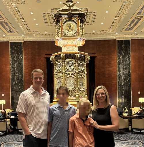 A family standing in from of the Peacock Alley Lounge at the Waldorf Astoria. A woman in a black dress, two boys and a man stand together.