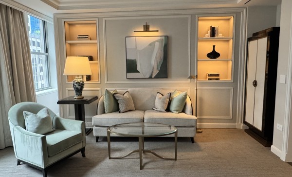 A beautiful seating area in the Waldorf Astoria's Jr Suite. There is are cream colored built in shelves with lighting, a cream colored couch and chairs, and a coffee table.