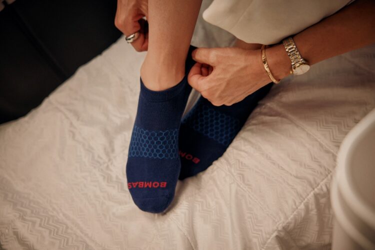 Detail of woman putting on Bombas Ankle socks in Delta one.